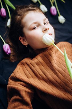 Kız karanlık bir arka planda lalelerin içinde yatıyor. Anneler Günün kutlu olsun.