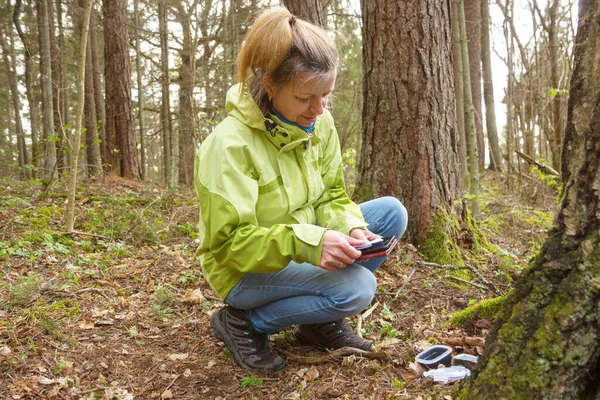 Uma mulher a fazer geocaching. Mulheres na floresta encontrar recipiente de geocache. Fotografia De Stock