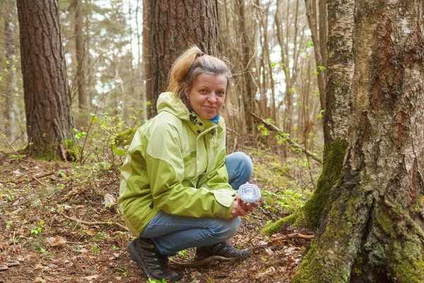 A woman geocaching. Women in woods find geocache container.