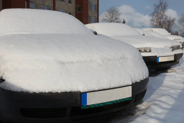 Snow covered cars parked in a row next to each other.