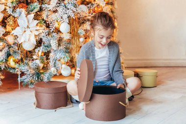 Noel arifesinde Noel ağacının yanında hediye kutusu olan küçük bir kız. Küçük çocuk kış dekorasyonlu, açık renk yatak odasında. Noel Yeni Yıl Kutlama Konsepti Zamanı