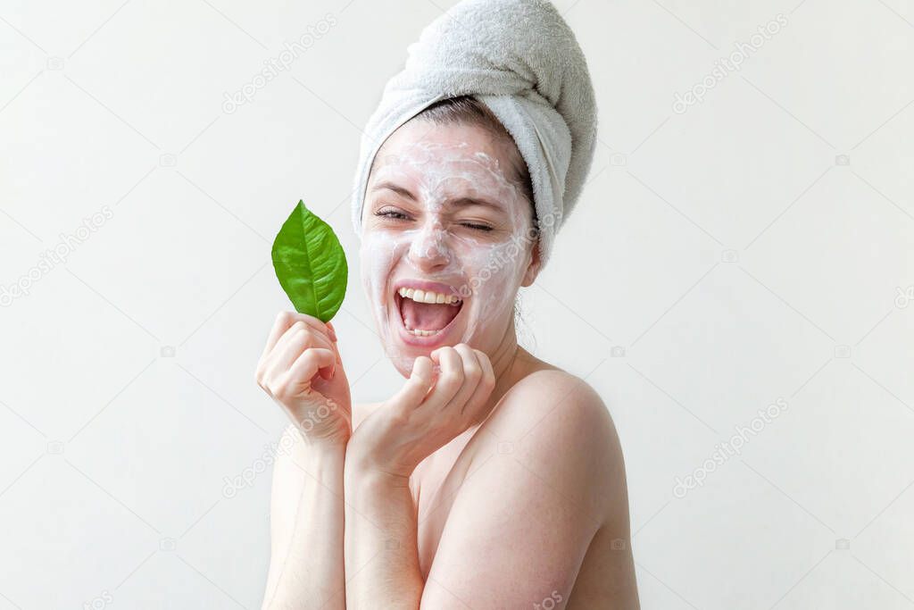 Minimal beauty portrait woman girl in towel on head applying white nourishing mask or creme on face, green leaf in hand isolated white background. Skincare cleansing eco organic cosmetic spa concept