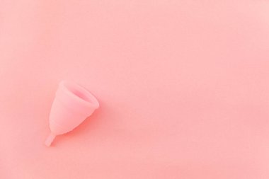 Pembe pastel arka planda izole edilmiş minimal tasarım adet bardağı. Adet döneminde modern kadın alternatif jinekolojik hijyen. Kan için konteynır. Düz görünüm kopyalama alanı