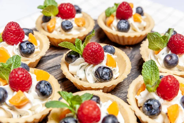 Tahta tepside çeşitli meyveli ve çilekli turtalar. Lezzetli hamur tatlısı turtalar taze ahududu ve peynir kremi ile renklendirilmiş pastalar. Fransız pastanesi.