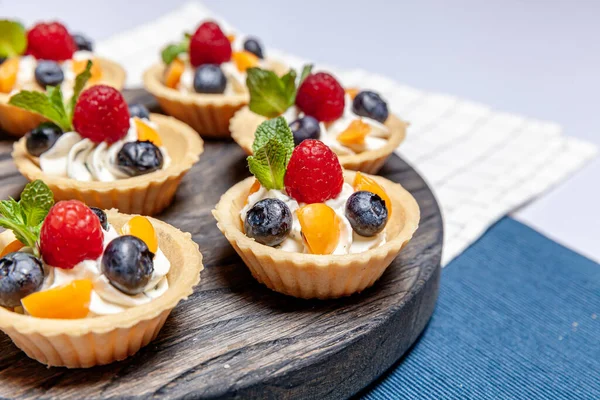 Tahta tepside çeşitli meyveli ve çilekli turtalar. Lezzetli hamur tatlısı turtalar taze ahududu ve peynir kremi ile renklendirilmiş pastalar. Fransız pastanesi.