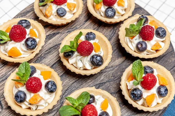 Tahta tepside çeşitli meyveli ve çilekli turtalar. Lezzetli hamur tatlısı turtalar taze ahududu ve peynir kremi ile renklendirilmiş pastalar. Fransız pastanesi.