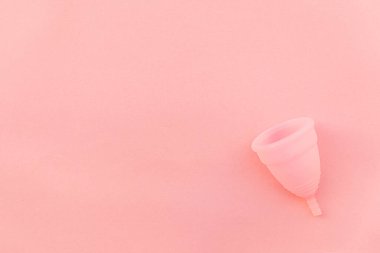Pembe pastel arka planda izole edilmiş minimal tasarım adet bardağı. Adet döneminde modern kadın alternatif jinekolojik hijyen. Kan için konteynır. Düz görünüm kopyalama alanı