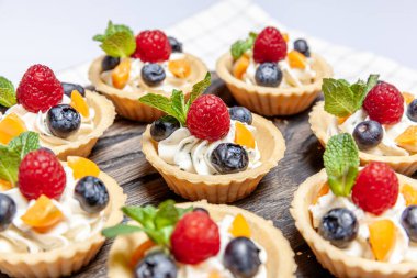 Tahta tepside çeşitli meyveli ve çilekli turtalar. Lezzetli hamur tatlısı turtalar taze ahududu ve peynir kremi ile renklendirilmiş pastalar. Fransız pastanesi.