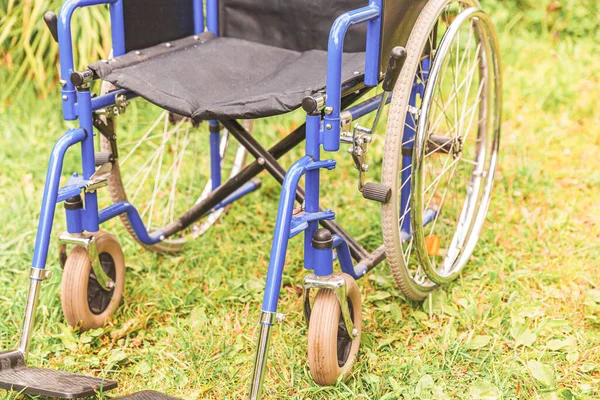 Empty wheelchair standing on grass in hospital park waiting for patient services. Invalid chair for disabled people parked outdoor in nature. Handicap accessible symbol. Health care medical concept