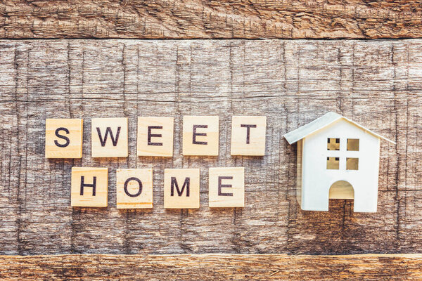 Miniature toy house with inscription SWEET HOME letters word on wooden background. Mortgage property insurance dream home concept. Flat lay top view copy space