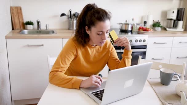 Frau kauft online ein und bezahlt mit Goldkarte. Junge Mädchen, die mit Laptop im Internet kaufen, geben Kreditkartendaten im Hintergrund der Küche ein. E-Commerce-Konzept für Online-Shopping. — Stockvideo