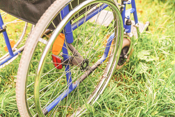 Пустое инвалидное кресло, стоящее на траве в больничном парке и ожидающее обслуживания пациентов. Инвалидное кресло для людей с ограниченными возможностями припарковано на природе. Символ доступный для инвалидов. Медицинская концепция