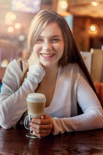 漂亮的少女微笑着坐在咖啡店或酒吧里 喝着拿铁咖啡玛奇朵 餐厅里拿着咖啡的女人 休息享受闲暇 喝咖啡休息早晨好 — 图库照片