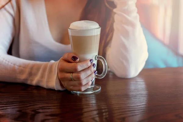 Latte macchiato drink in tall glass close up. Coffee fresh cream cappuccino on table in cafe. Wake up, morning addiction concept.