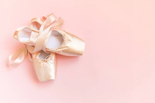 New pastel beige ballet shoes with satin ribbon isolated on pink background. Ballerina classical pointe shoes for dance training. Ballet school concept. Top view flat lay copy space