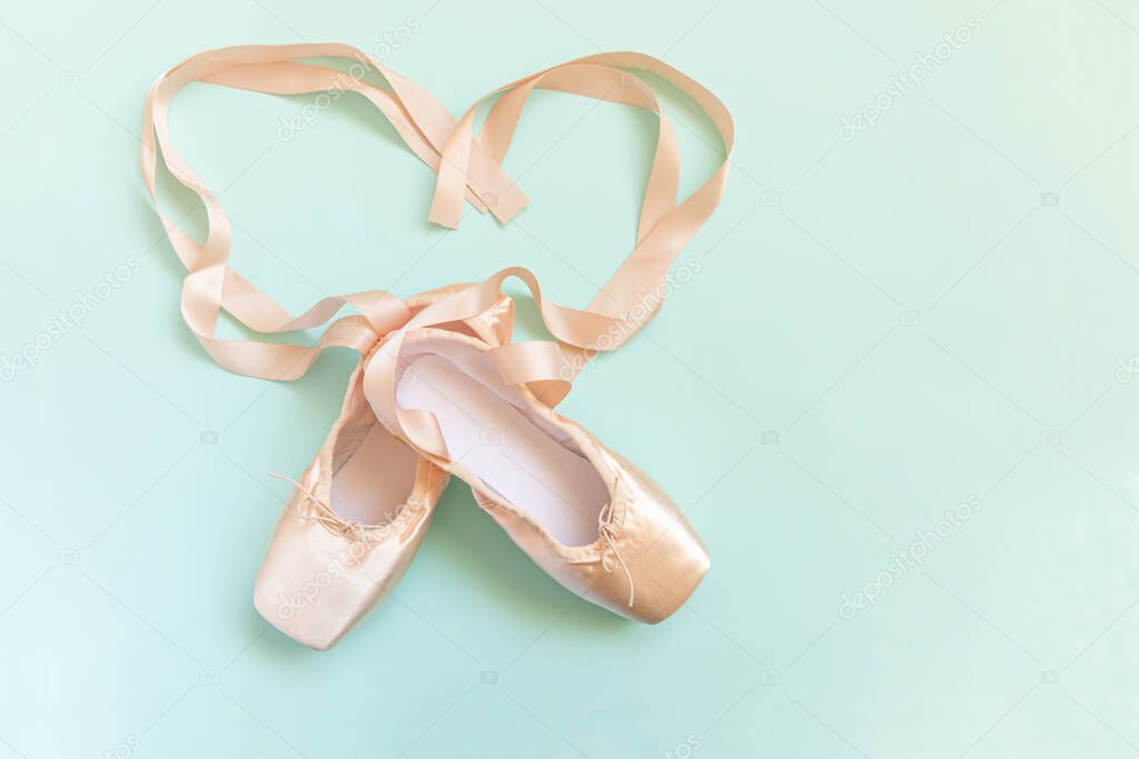 New pastel beige ballet shoes with satin ribbon isolated on blue background. Ballerina classical pointe shoes for dance training. Ballet school concept. Top view flat lay copy space