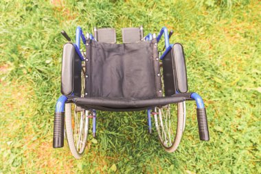 Hastane parkında çimlerde bekleyen boş tekerlekli sandalye hasta hizmetlerini bekliyor. Doğada park etmiş engelliler için geçersiz sandalye. Özürlü erişilebilir sembol. Sağlık hizmeti tıbbi konsepti