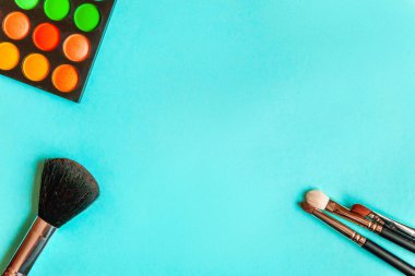 Makyaj ve kozmetik için farklı göz falı tonları ve renkli mavi pastel arka planda makyaj fırçası. Üst görünüm düz yatay ve resim gibi