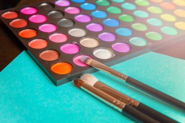 Makyaj ve kozmetik için farklı göz falı tonları ve renkli mavi pastel arka planda makyaj fırçası. Üst görünüm düz yatay ve resim gibi