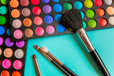 Makyaj ve kozmetik için farklı göz falı tonları ve renkli mavi pastel arka planda makyaj fırçası. Üst görünüm düz yatay ve resim gibi