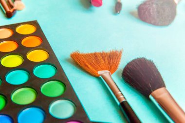 Makyaj ve kozmetik için farklı göz falı tonları ve renkli mavi pastel arka planda makyaj fırçası. Üst görünüm düz yatay ve resim gibi
