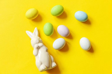 Mutlu Paskalyalar. Tatil için hazırlık. Paskalya çikolatalı yumurta, tatlı ve sarı arka planda izole edilmiş tavşan oyuncağı. Basit minimalizm düz üst görünüm kopyalama alanı