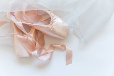 Beyaz arka planda saten kurdeleli ve etekli yeni pastel bej bale ayakkabıları. Dans eğitimi için klasik balerin ayakkabıları. Bale okulu konsepti. Üst görünüm düz kopya alanı