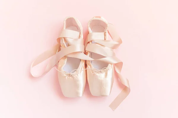 New pastel beige ballet shoes with satin ribbon isolated on pink background. Ballerina classical pointe shoes for dance training. Ballet school concept. Top view flat lay copy space