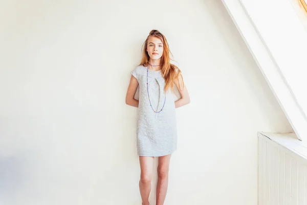 Feliz adolescente sonriendo. Retrato joven feliz adolescente positivo mujer en vestido gris en casa en habitación luminosa contra la pared blanca. Mujer europea. Emoción humana positiva expresión facial lenguaje corporal. — Foto de Stock