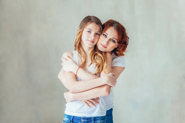 Jonge moeder die haar kind omarmt. Vrouw en tienermeisje ontspannen in witte slaapkamer in de buurt van grijze muur binnen. Gelukkig gezin thuis. jong mam spelen met haar dochter. — Stockfoto