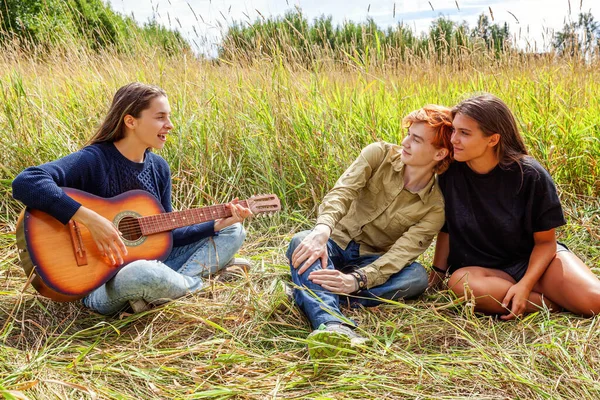 Summer holidays vacation music happy people concept. Group of three friends boy and two girls with guitar singing song having fun together outdoors. Picnic with friends on road trip in nature.