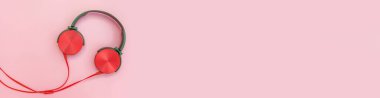 Pembe arka planda kırmızı kulaklıklar. Fotokopi alanı ve pankartı olan basit kulaklıkların minimalist fotoğrafı. Renkli arka planda kabloyla izole edilmiş kırmızı DJ kulaklıklar, düz manzara. Müzik konsepti