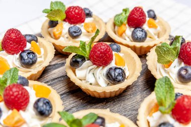 Tahta tepside çeşitli meyveli ve çilekli turtalar. Lezzetli hamur tatlısı turtalar taze ahududu ve peynir kremi ile renklendirilmiş pastalar. Fransız pastanesi.