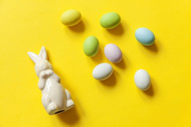 Mutlu Paskalyalar. Tatil için hazırlık. Paskalya çikolatalı yumurta, tatlı ve sarı arka planda izole edilmiş tavşan oyuncağı. Basit minimalizm düz üst görünüm kopyalama alanı