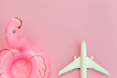 Yaz kumsalı kompozisyonu. Uçak ve pastel pembe arka planda izole edilmiş şişme flamingo ile minimum sade düz yatıyordu. Seyahat macerası konsepti. Üst görünüm kopyalama alanı
