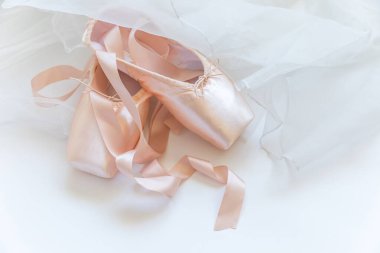 Beyaz arka planda saten kurdeleli ve etekli yeni pastel bej bale ayakkabıları. Dans eğitimi için klasik balerin ayakkabıları. Bale okulu konsepti. Üst görünüm düz kopya alanı