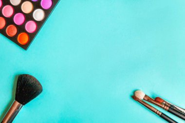 Makyaj ve kozmetik için farklı göz falı tonları ve renkli mavi pastel arka planda makyaj fırçası. Üst görünüm düz yatay ve resim gibi