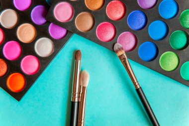 Makyaj ve kozmetik için farklı göz falı tonları ve renkli mavi pastel arka planda makyaj fırçası. Üst görünüm düz yatay ve resim gibi