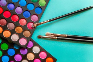 Makyaj ve kozmetik için farklı göz falı tonları ve renkli mavi pastel arka planda makyaj fırçası. Üst görünüm düz yatay ve resim gibi