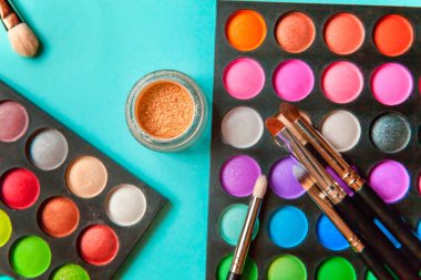 Makyaj ve kozmetik için farklı göz falı tonları ve renkli mavi pastel arka planda makyaj fırçası. Üst görünüm düz yatay ve resim gibi