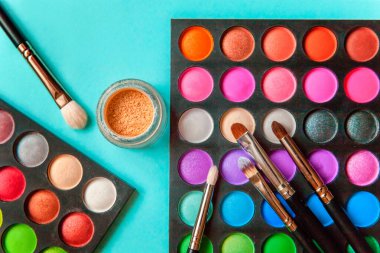 Makyaj ve kozmetik için farklı göz falı tonları ve renkli mavi pastel arka planda makyaj fırçası. Üst görünüm düz yatay ve resim gibi