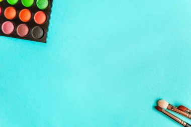 Makyaj ve kozmetik için farklı göz falı tonları ve renkli mavi pastel arka planda makyaj fırçası. Üst görünüm düz yatay ve resim gibi