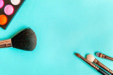 Makyaj ve kozmetik için farklı göz falı tonları ve renkli mavi pastel arka planda makyaj fırçası. Üst görünüm düz yatay ve resim gibi
