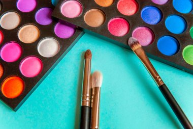 Makyaj ve kozmetik için farklı göz falı tonları ve renkli mavi pastel arka planda makyaj fırçası. Üst görünüm düz yatay ve resim gibi