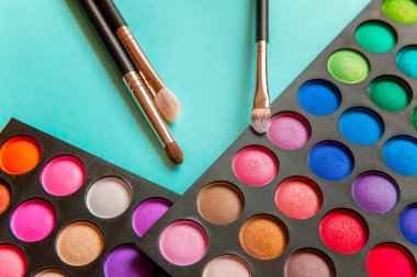 Makyaj ve kozmetik için farklı göz falı tonları ve renkli mavi pastel arka planda makyaj fırçası. Üst görünüm düz yatay ve resim gibi