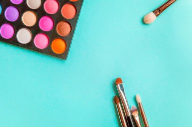 Makyaj ve kozmetik için farklı göz falı tonları ve renkli mavi pastel arka planda makyaj fırçası. Üst görünüm düz yatay ve resim gibi