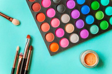 Makyaj ve kozmetik için farklı göz falı tonları ve renkli mavi pastel arka planda makyaj fırçası. Üst görünüm düz yatay ve resim gibi