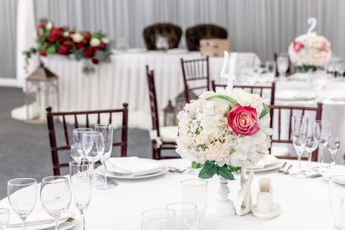 Restoranda çiçek kompozisyonu olan lüks bir masa, iç mekan. Şık bir düğün ziyafeti dekorasyonu ve yemek servisi tarafından beyaz masada hazırlanan eşyalar.