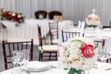 Restoranda çiçek kompozisyonu olan lüks bir masa, iç mekan. Şık bir düğün ziyafeti dekorasyonu ve yemek servisi tarafından beyaz masada hazırlanan eşyalar..