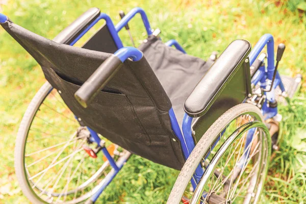 Empty wheelchair standing on grass in hospital park waiting for patient services. Invalid chair for disabled people parked outdoor in nature. Handicap accessible symbol. Health care medical concept